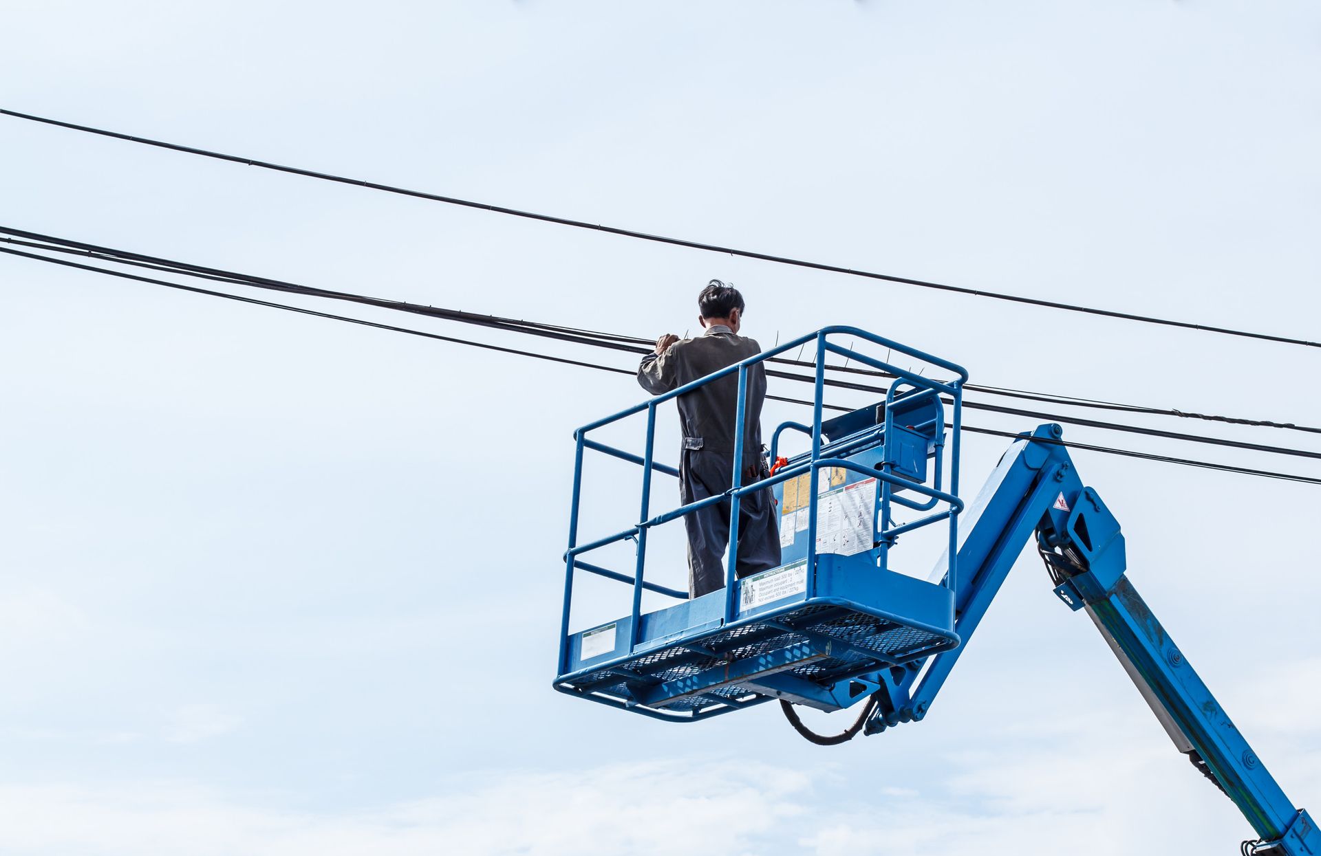 Dos trabajadores de la construcción en un ascensor amarillo trabajando en una cerca de alambre contra un cielo azul con nubes.