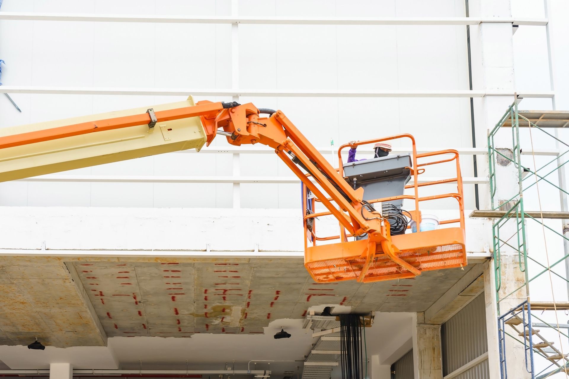 Un trabajador de la construcción con casco amarillo y arnés en un elevador, inspeccionando una estructura metálica grande y curva.