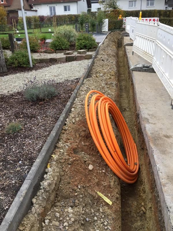 Ein Glasfaserkabel liegt im Dreck neben einem Gehweg.