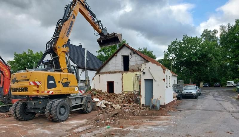 Ein gelber Bagger zerstört auf einer Baustelle ein Gebäude.
