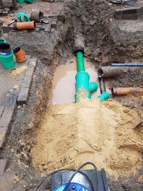 In einem Loch im Boden wird ein grünes Rohr installiert.