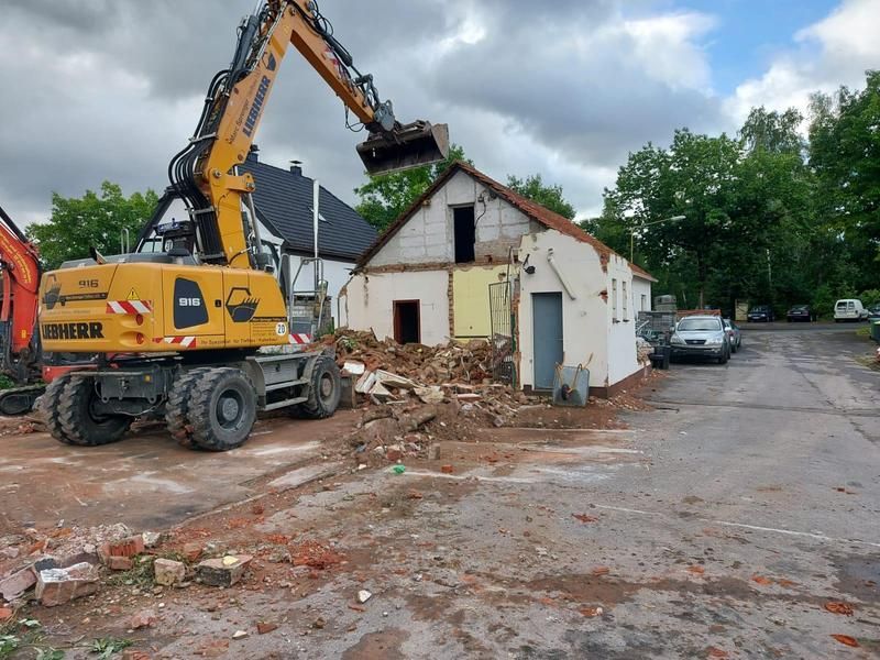 Ein gelber Bagger zerstört ein Gebäude auf einem Parkplatz.