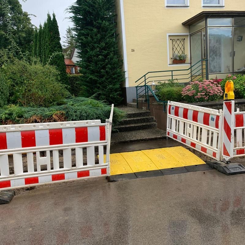 Eine rot-weiß-gelbe Barriere blockiert eine gelbe Rampe vor einem Haus