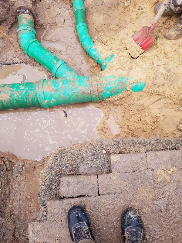 Eine Person steht neben einem grünen Rohr im Dreck.