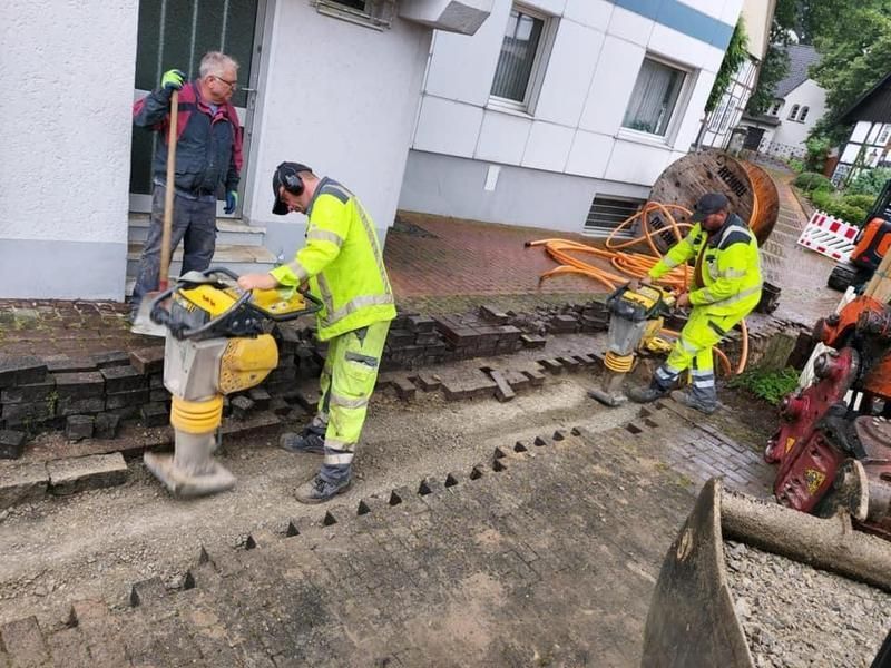 Eine Gruppe Bauarbeiter arbeitet an einem Gehweg vor einem Gebäude.