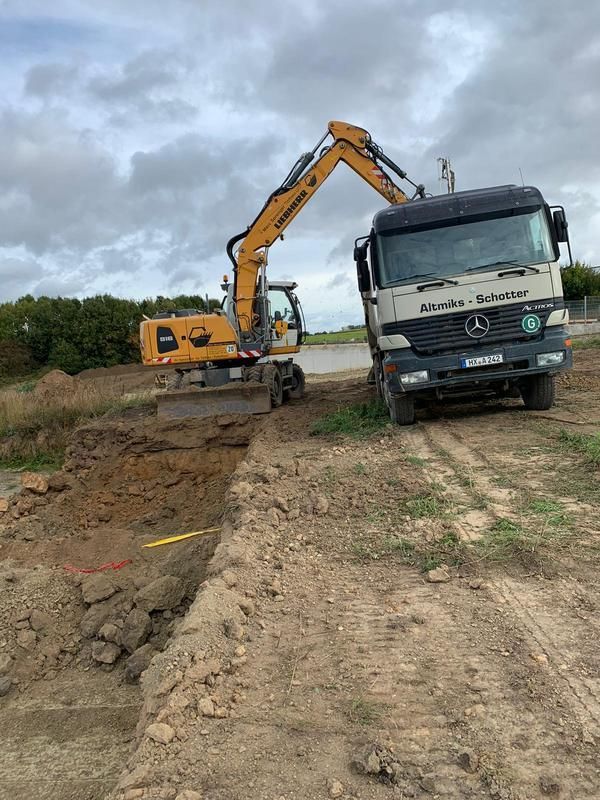 Ein Lastwagen fährt auf einer unbefestigten Straße neben einem Bagger her.
