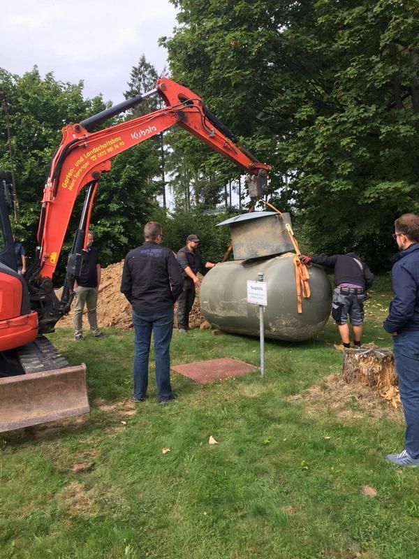 Eine Gruppe von Menschen steht um einen großen Tank herum, der gerade von einem Kran angehoben wird.