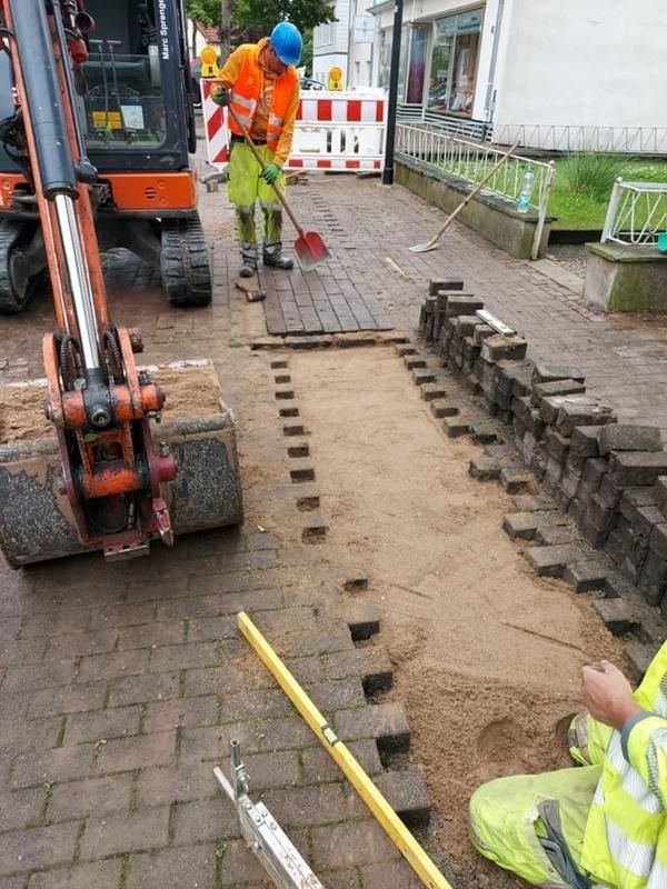 Ein Mann legt Ziegelsteine auf einem Gehweg neben einem Bulldozer.