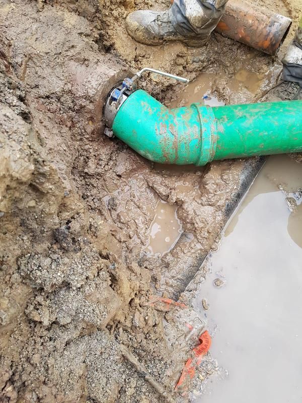 Ein grünes Rohr liegt im Schlamm neben einer Pfütze.