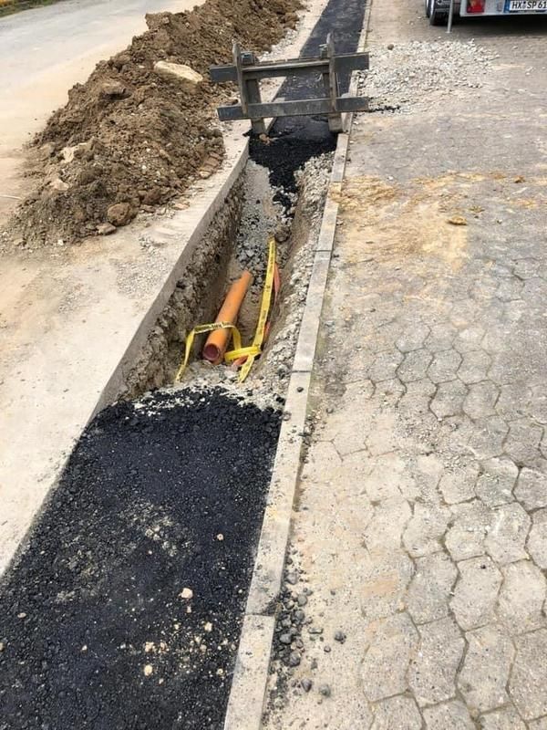 Ein gelbes Rohr liegt im Dreck neben einem Betonbordstein.