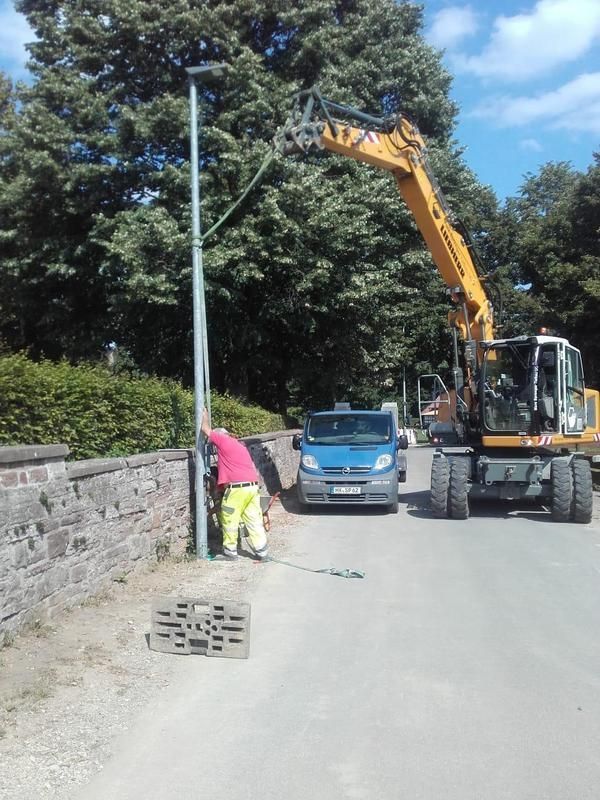 Ein gelber Bagger arbeitet an einer Straßenlaterne
