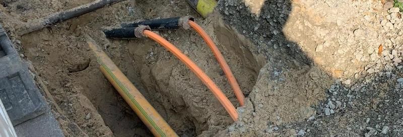 Ein paar orangefarbene Glasfaserkabel liegen im Dreck.