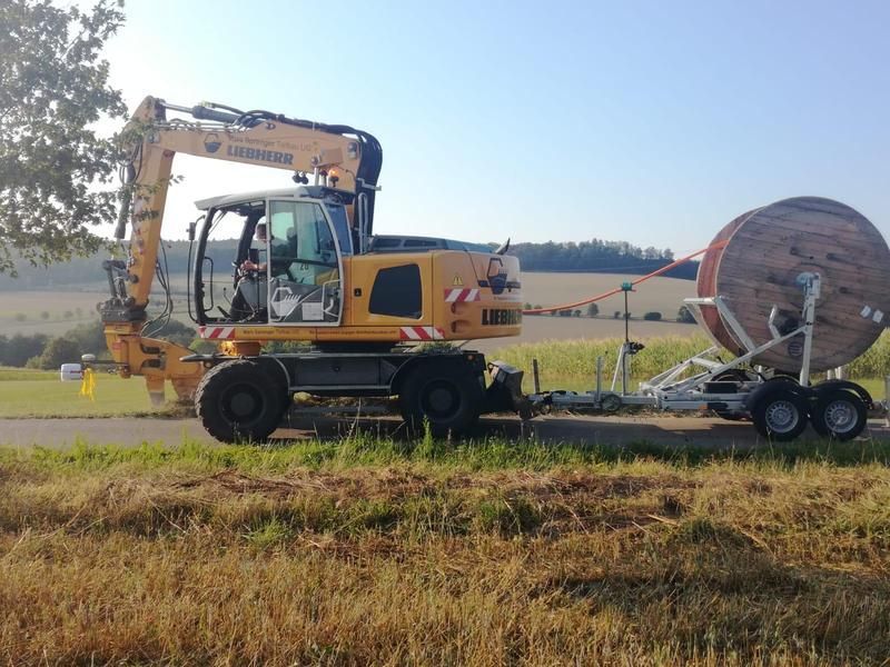 Ein gelber Bagger transportiert eine große Kabelspule auf einem Anhänger.