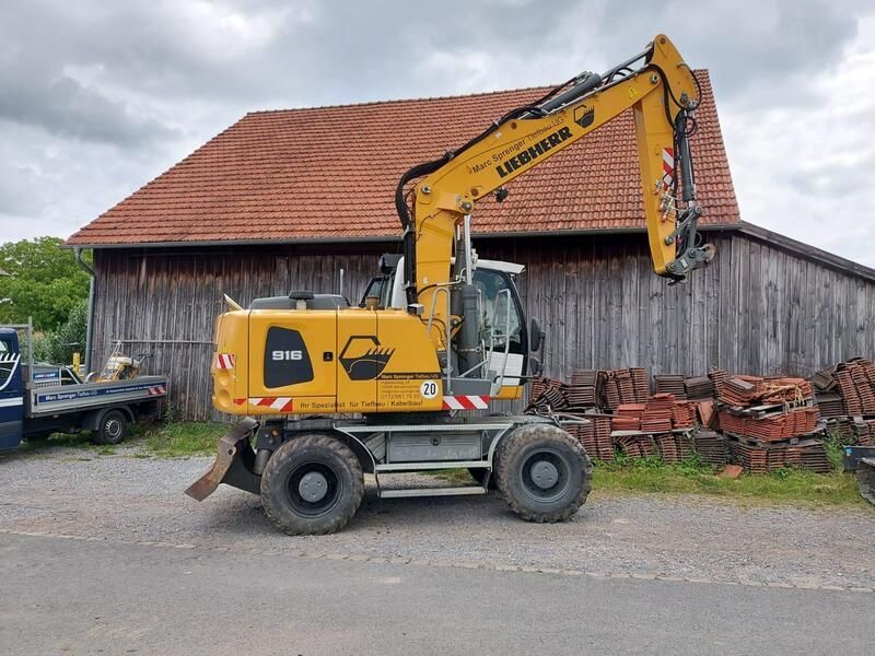 Vor einem Holzgebäude parkt ein gelber Bagger.