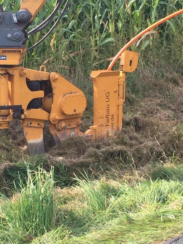 Ein gelber Traktor gräbt ein Loch ins Gras.