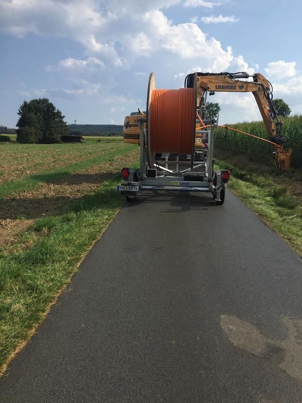 Eine große Kabelspule wird von einem großen Bagger auf einem Anhänger gezogen.
