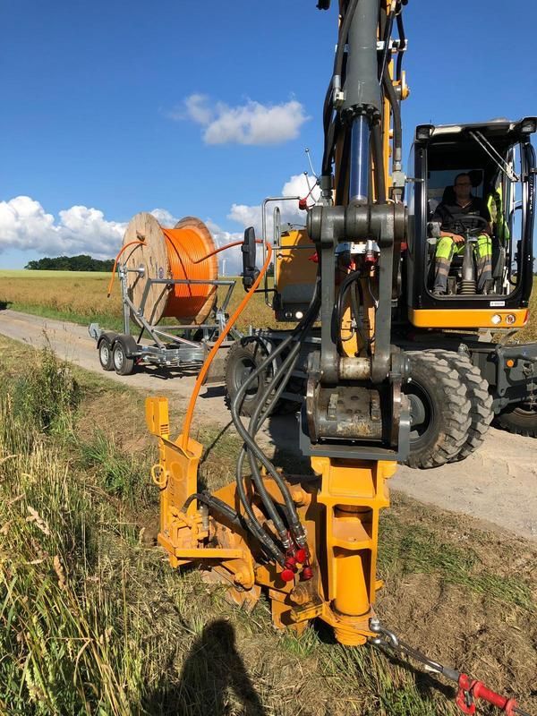 Ein Mann fährt einen gelben Bagger auf einer unbefestigten Straße.