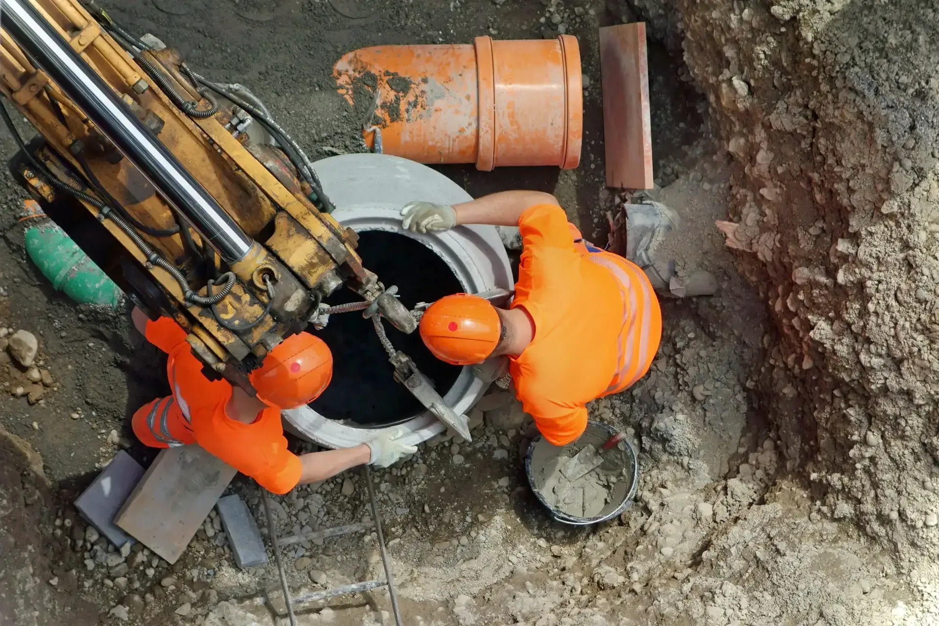 Zwei Bauarbeiter arbeiten im Erdreich an einem Gullydeckel.