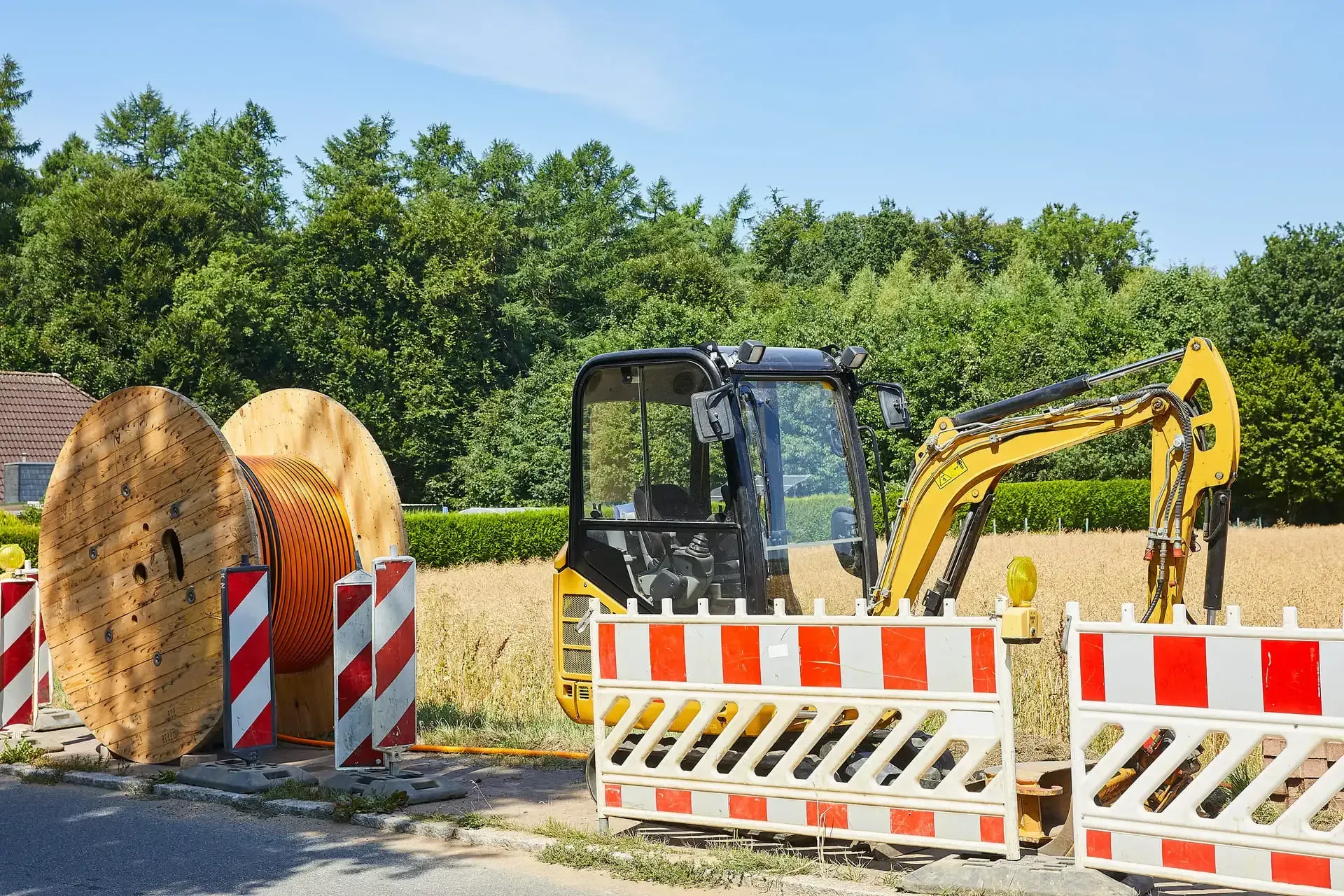 Eine Baustelle mit einem gelben Bagger und einer großen Spule Glasfaserkabel.