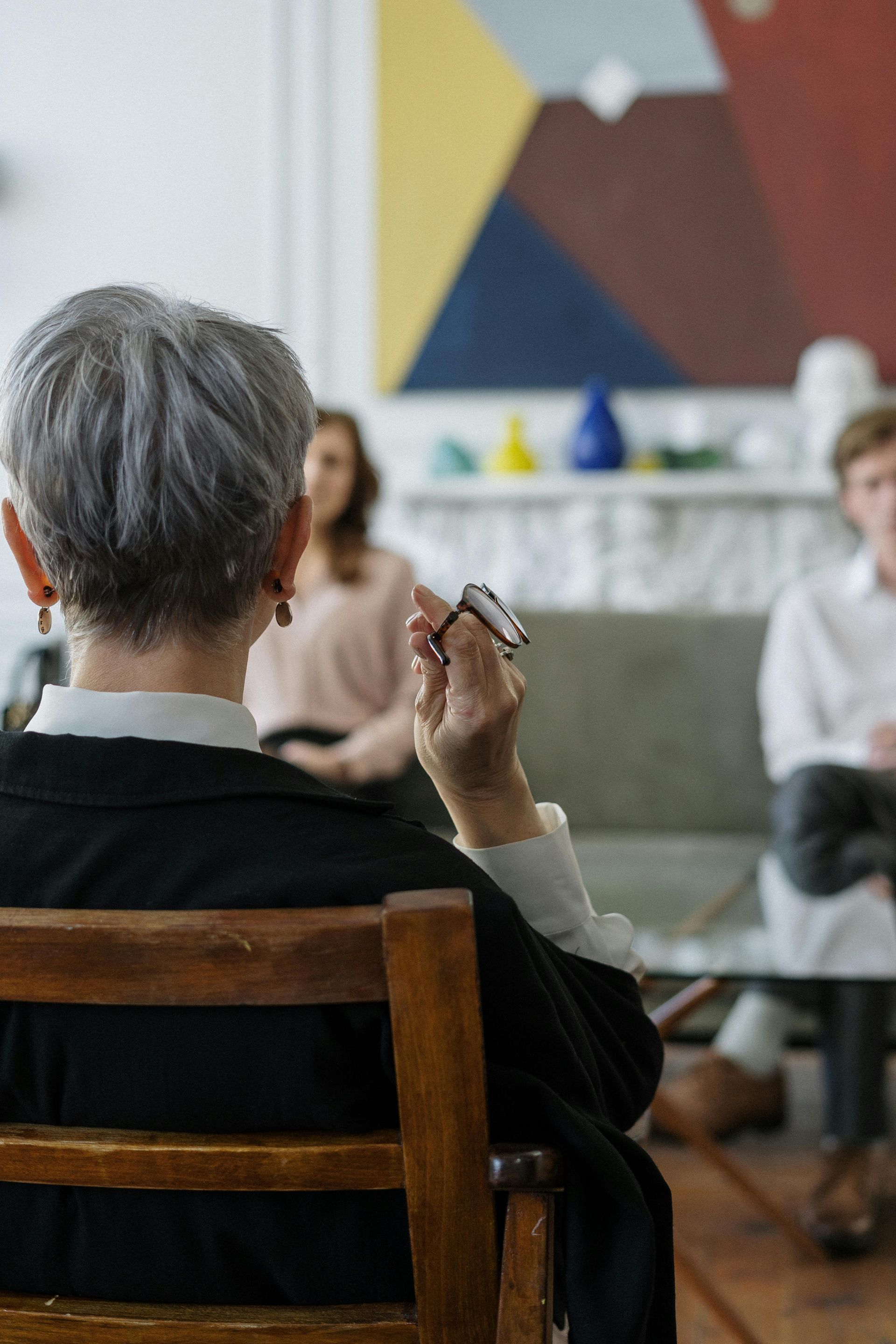 Consejero de cabello gris sosteniendo un bolígrafo, frente a dos personas en un sofá.