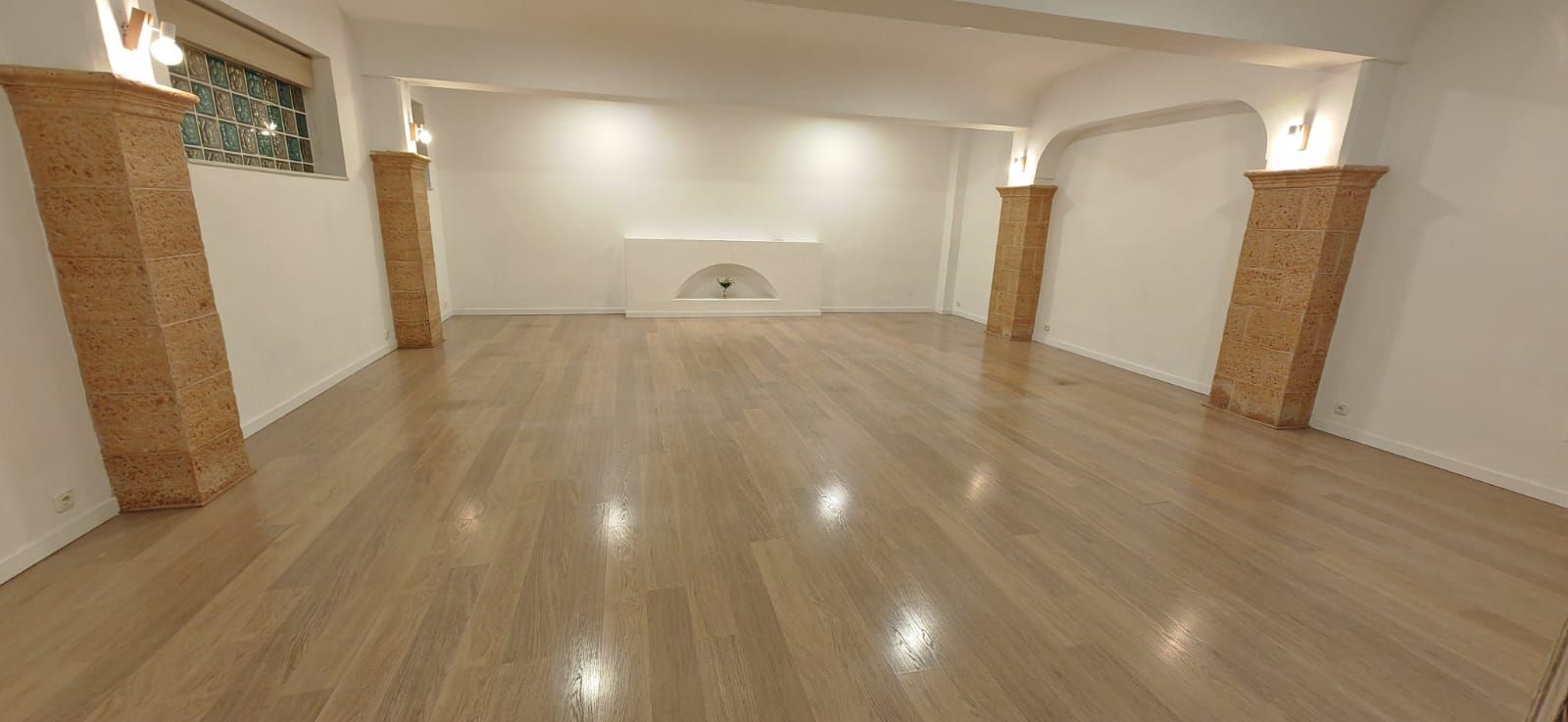 Sala de estar beige con sofá, silla, plantas, obras de arte y lámpara de pie.