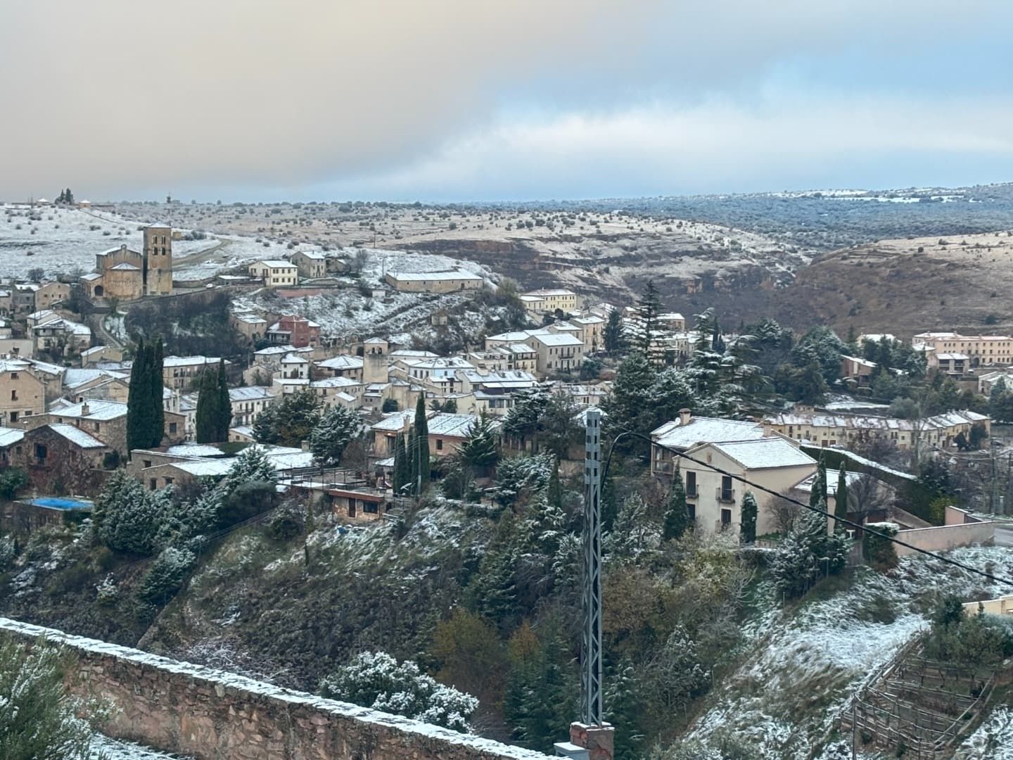 Pueblo nevado en una ladera bajo un cielo nublado. Edificios y árboles salpican el paisaje.