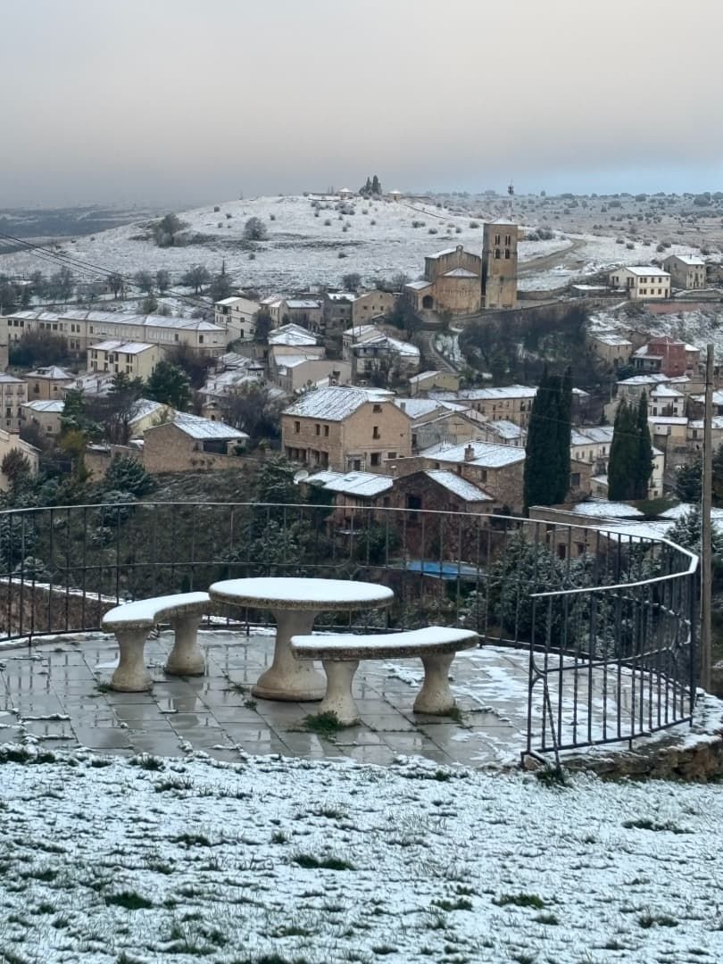 Pueblo nevado con mesas de piedra, iglesia y edificios en la cima de una colina. Cielo nublado.