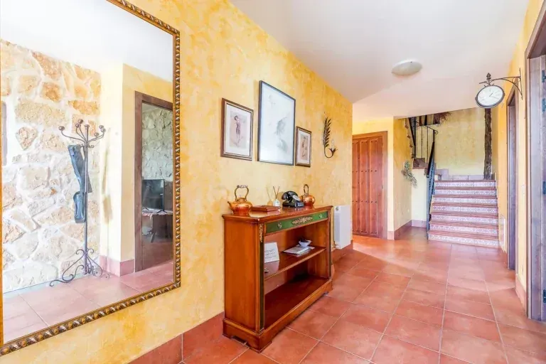 Pasillo con paredes amarillas, suelo de baldosas rojas, consola de madera, espejo y escalera.