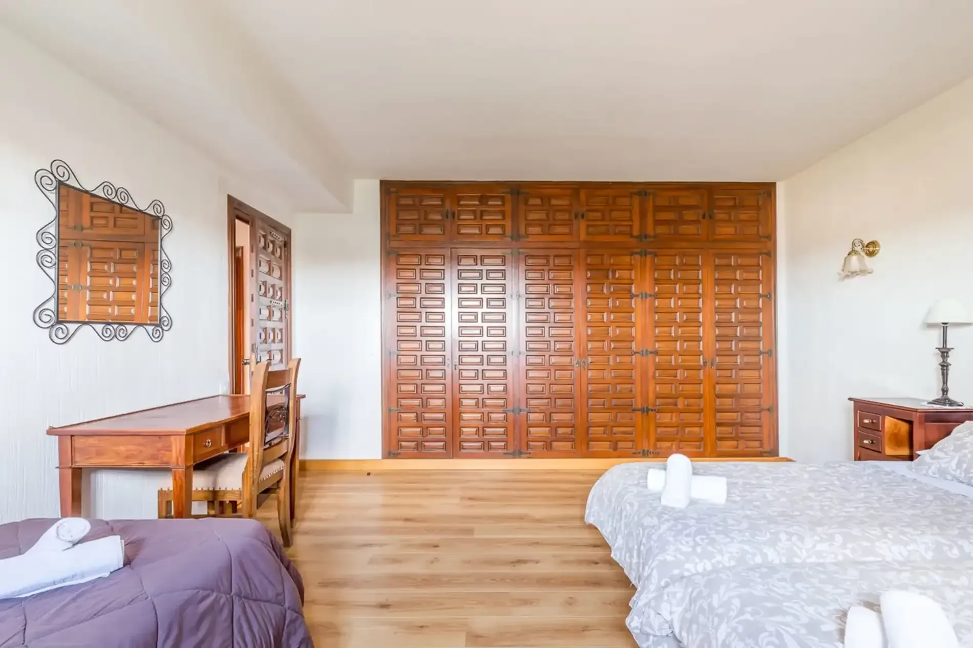 Dormitorio con armario de madera, escritorio y dos camas; paredes blancas, suelo de madera.