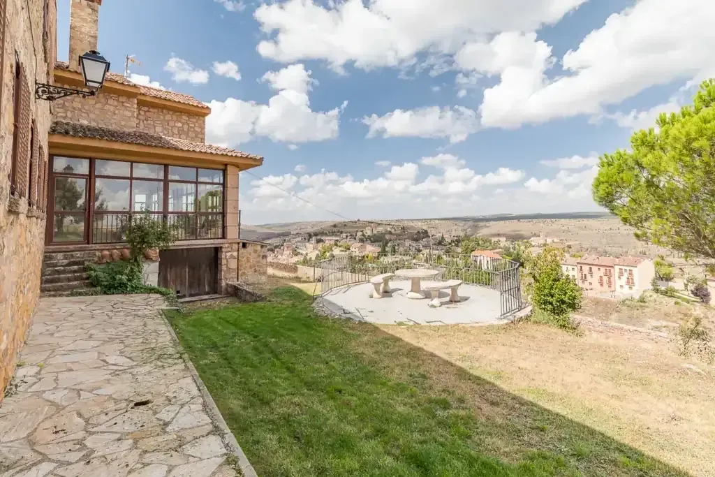 Un edificio con un porche acristalado da a un paisaje soleado con un patio de piedra y una mesa de picnic.