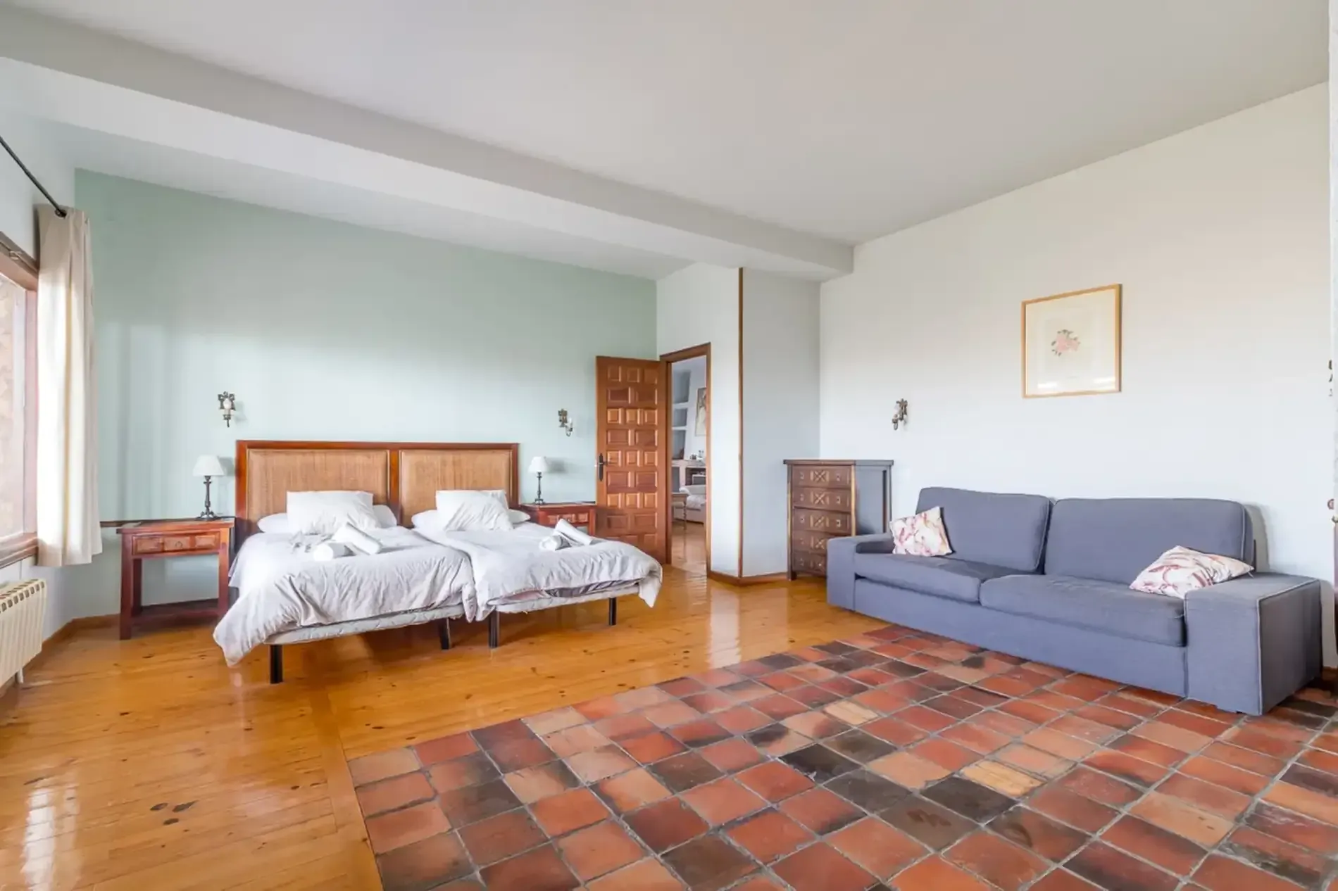 Dormitorio con dos camas individuales, sofá, suelo de madera y alfombra de baldosas.