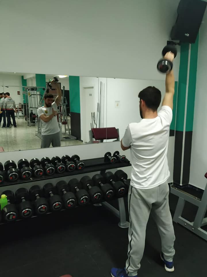 Un hombre está levantando una mancuerna frente a un espejo en un gimnasio.