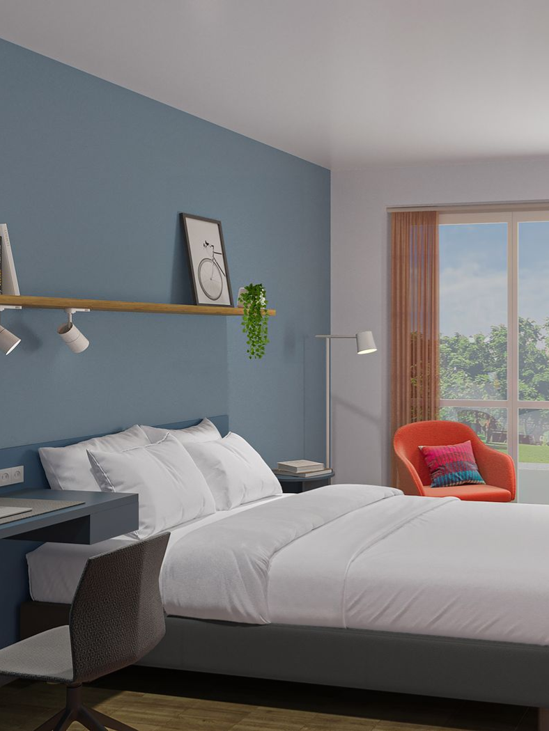 Schlafzimmer mit Bett, Schreibtisch, Stuhl, Fenster mit Stuhl und einem an der Wand montierten Fernseher.