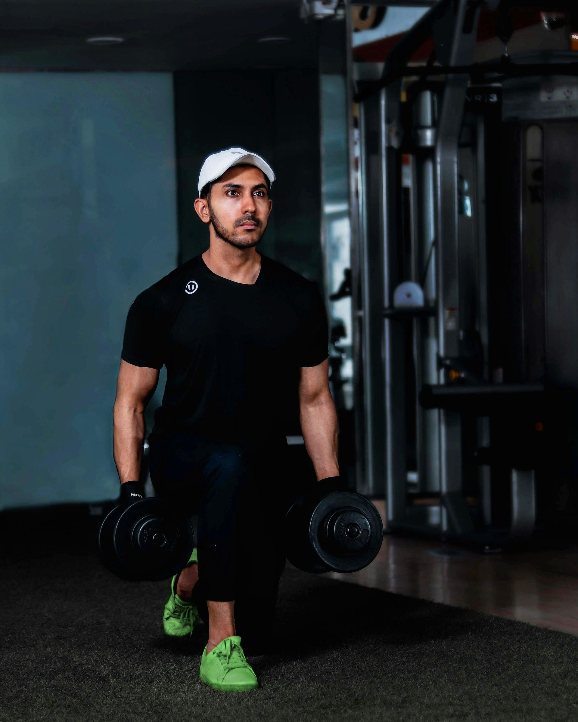 Ein Mann in schwarzer Sportkleidung macht Ausfallschritte mit Kurzhanteln im Fitnessstudio.