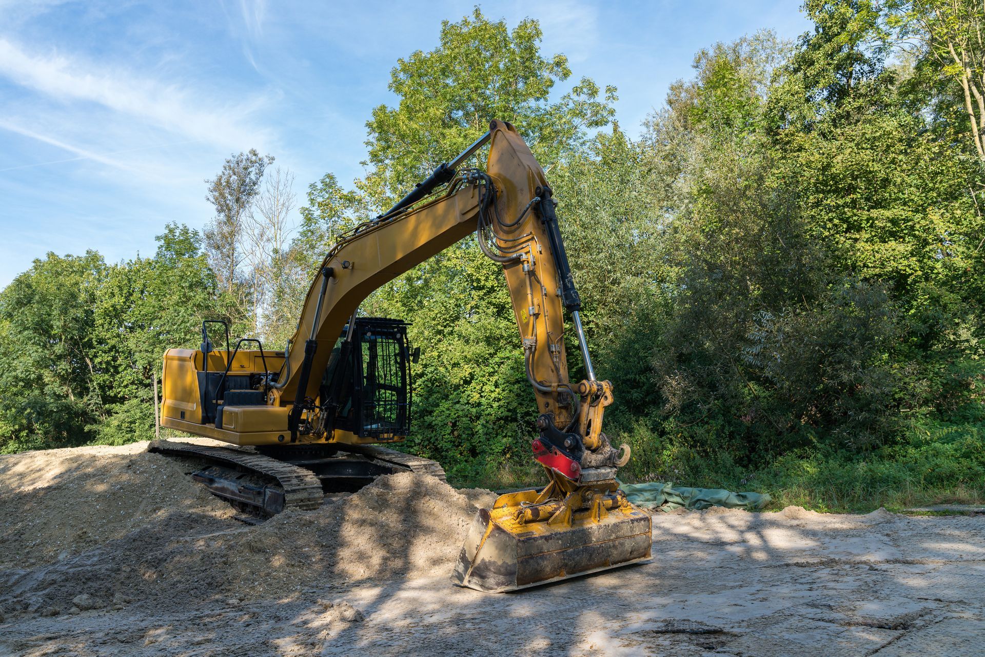 Excavateur sur un tas de gravier, travaillant près des arbres.