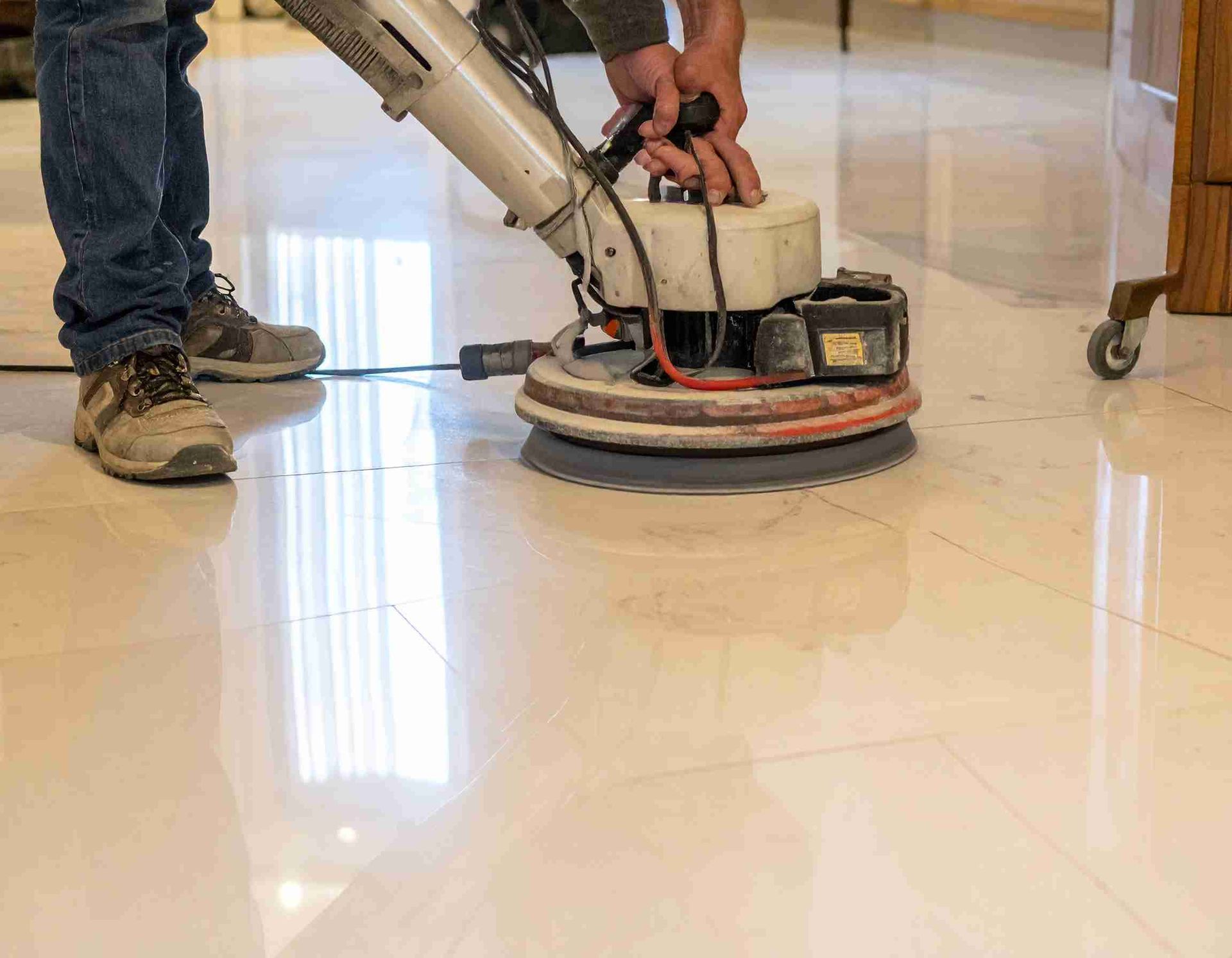 Una persona utiliza una máquina pulidora de pisos sobre un piso de baldosas brillantes y de color claro.