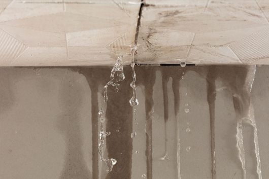 De l’eau s’infiltre par un plafond fissuré et ruisselle le long d’un mur.