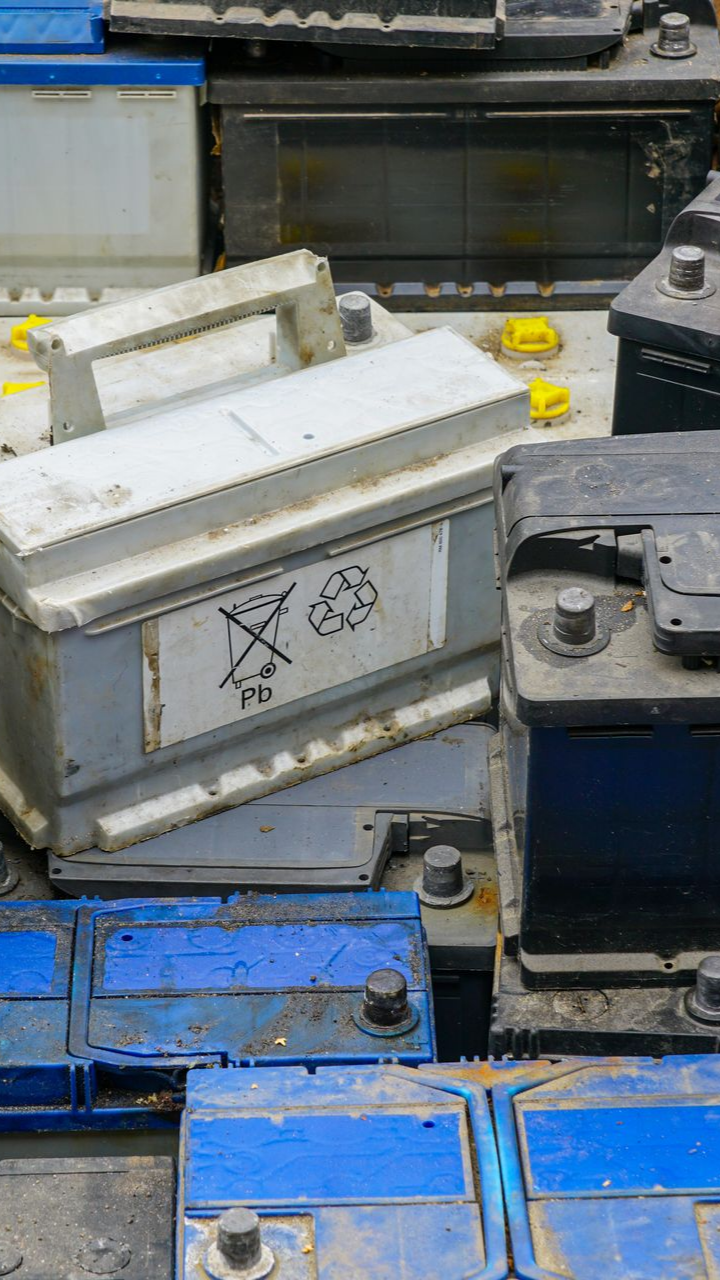 Pile de batteries automobiles usagées, principalement grises et bleues, portant des symboles de recyclage.