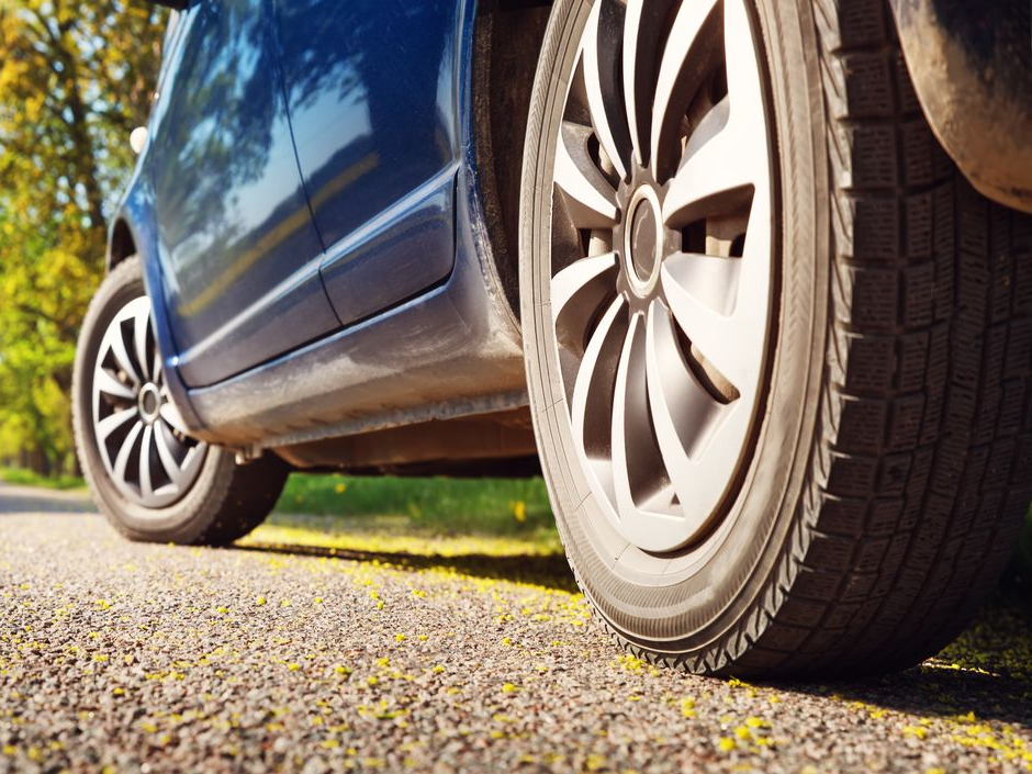 Pneus d'une voiture bleue sur une route asphaltée. Gros plan sur les roues et la carrosserie, avec de la verdure en arrière-plan.