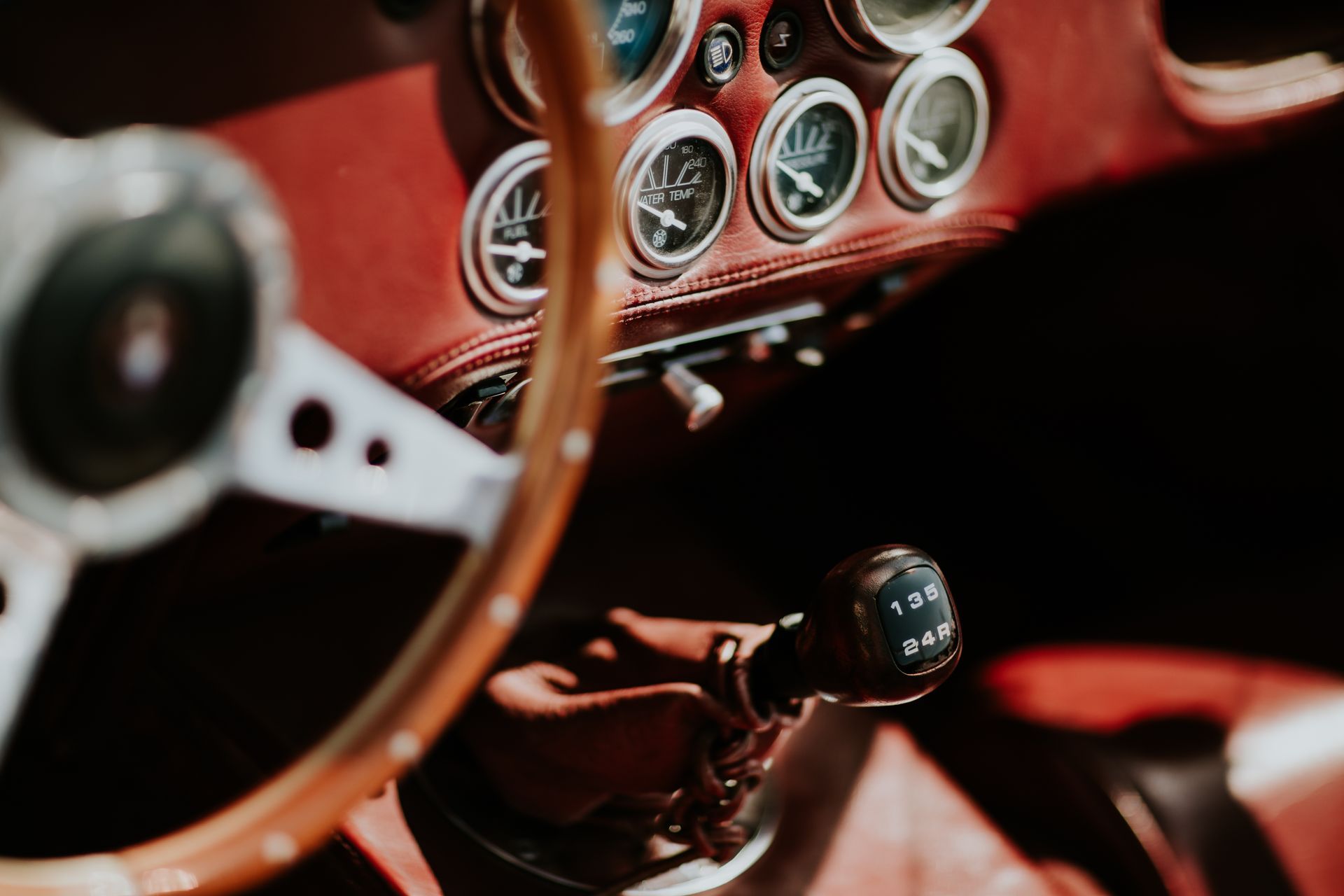 Intérieur d'une voiture classique : volant en bois, tableau de bord en cuir rouge, cadrans, levier de vitesses en main.
