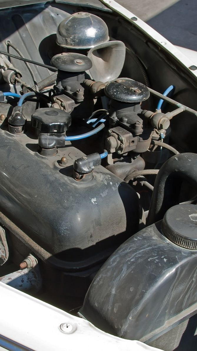 Gros plan sur un vieux moteur de voiture, composants noirs et argentés avec des fils de bougie bleus.