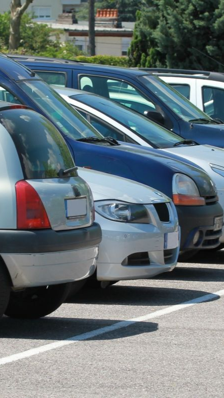 Voitures garées en rang dans un parking par une journée ensoleillée.