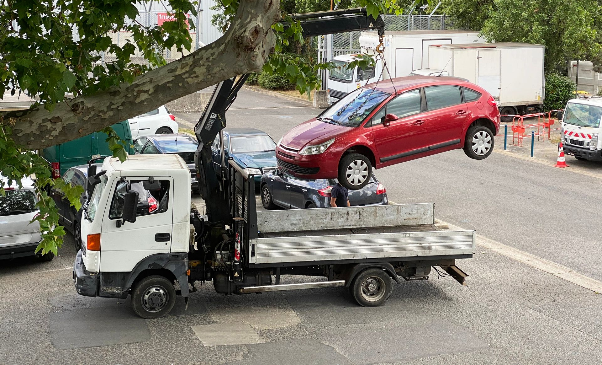 Voiture rouge soulevée par une grue et placée sur le plateau d'un camion de remorquage.
