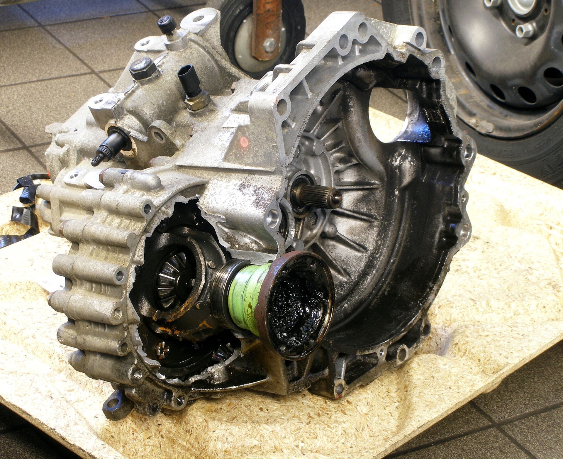 Boîte de vitesses de voiture endommagée, carter métallique, recouverte d'huile, sur une surface de travail.