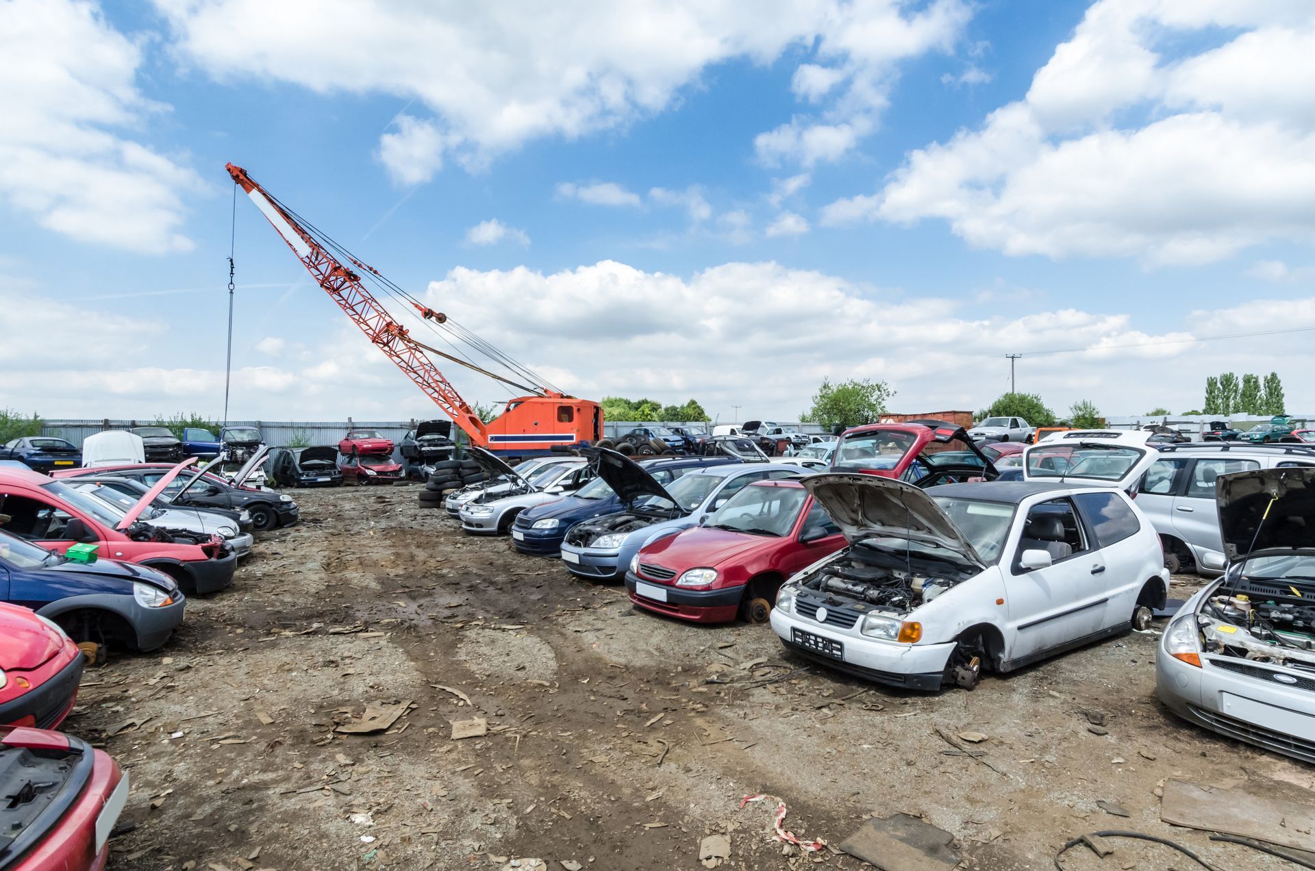 Des voitures dans une casse, une grue orange sous un ciel bleu.