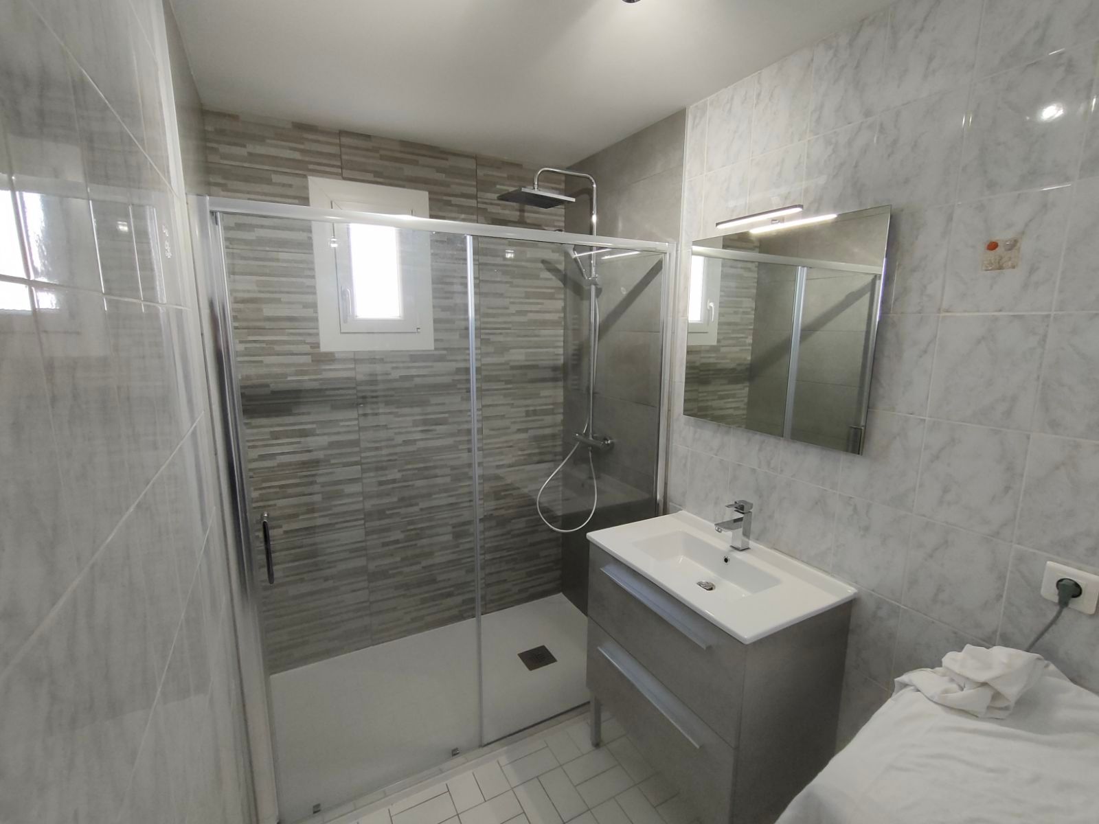 Salle de bains grise avec receveur, paroi, meuble et miroir