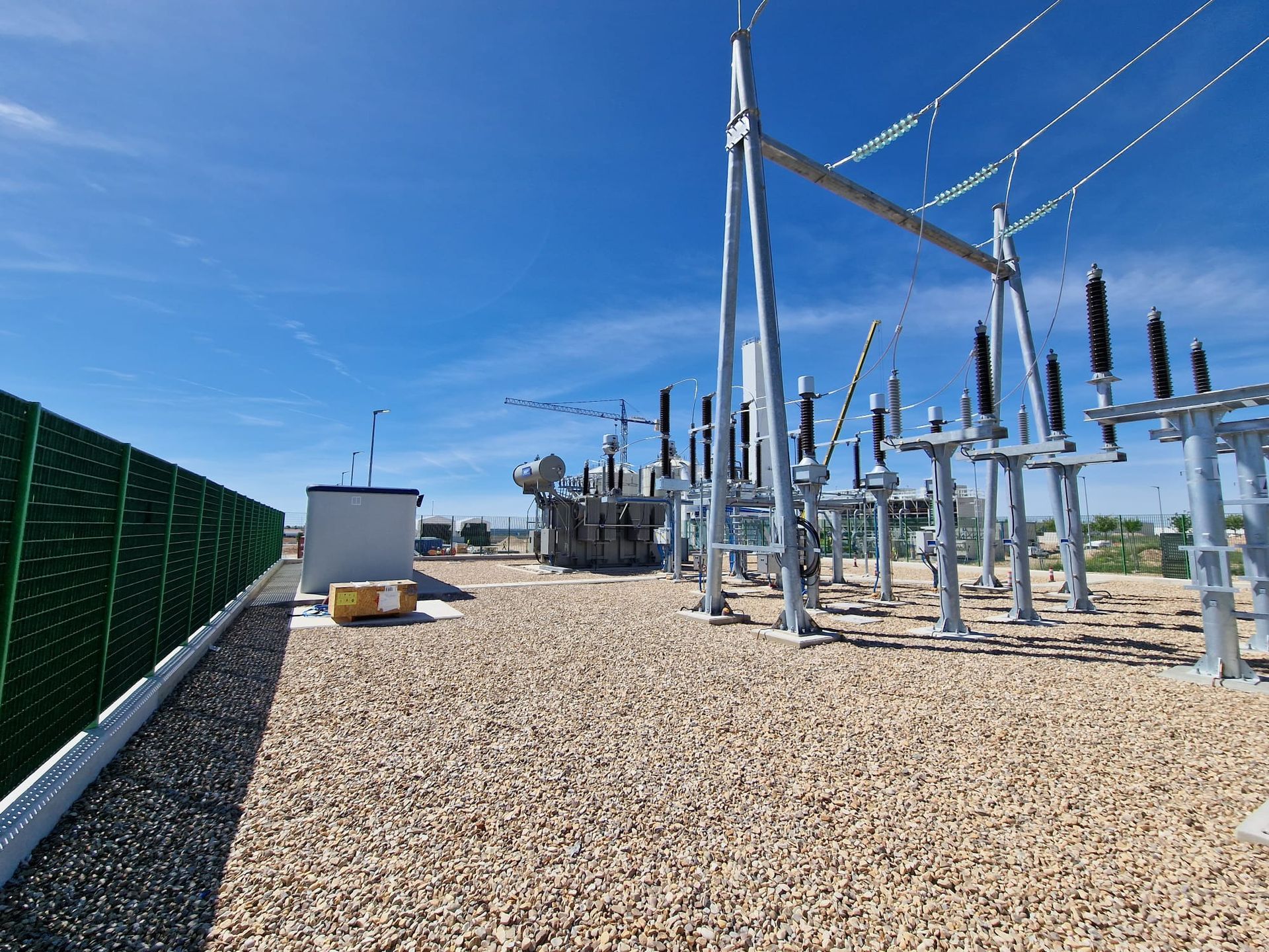 Subestación eléctrica al aire libre sobre una superficie de grava bajo un cielo azul.