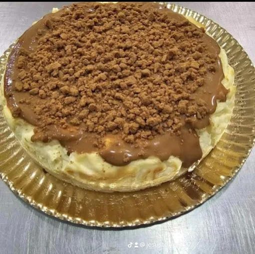 Una tarta de queso con salsa de chocolate y migas encima está en un plato de papel.