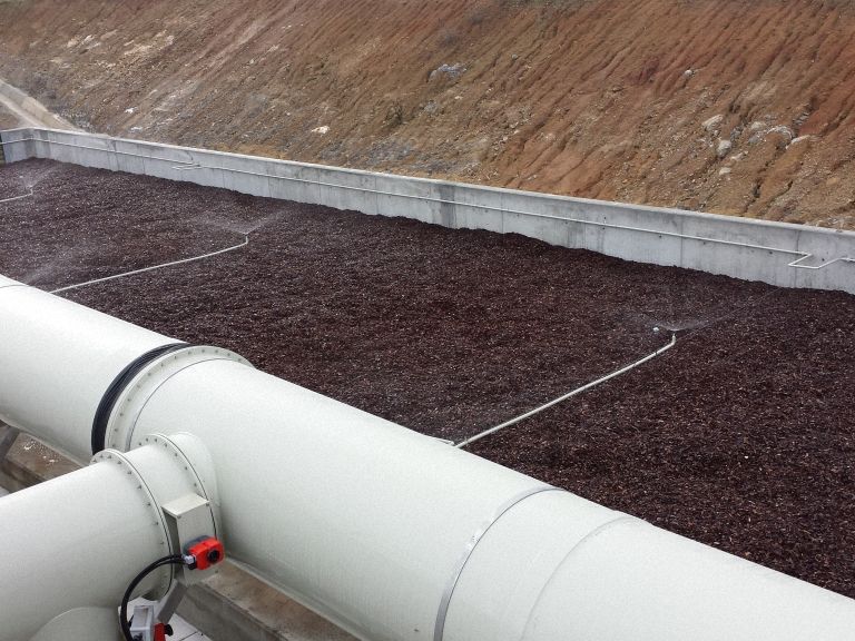 Gran estanque rectangular para tratamiento de agua, lleno de medios de color marrón rojizo oscuro, paredes de hormigón.