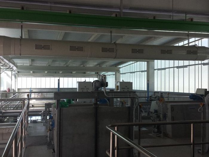 Dentro de una nave industrial, estructura de hormigón con maquinaria y ventilación, con ventanas al fondo.
